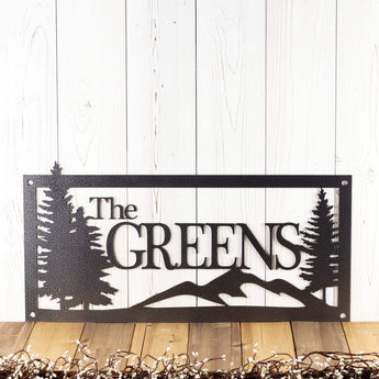 Rectangular personalized metal family name sign, with pine trees and mountain range, in silver vein powder coat. 
