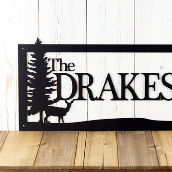 Close up of rectangular family name metal plaque with a doe deer and pine trees, in matte black powder coat. 