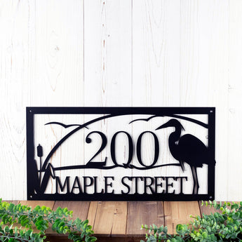 Close up of rectangular metal address sign with great blue heron, cattails, and and sunset lake scene, in matte black powder coat.