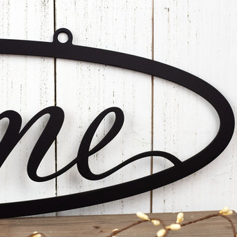 Close up of script lettering on our hanging oval Home metal wall art, in matte black powder coat. 