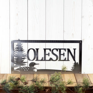 Rectangular metal family last name sign with loon and pine trees, in raw steel.