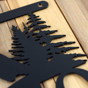 Close up of matte black powder coat on our hanging metal house number sign with pine trees and mountains. 