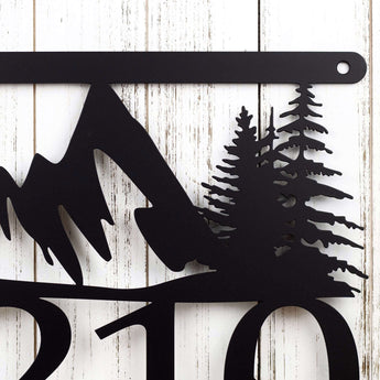 Close up of mountains and pine trees on our hanging metal house number sign, in matte black powder coat.