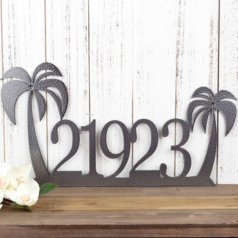 5 digit metal house number sign with palm trees, in silver vein powder coat. Placed against a white wood wall.