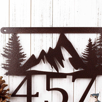 Close up of mountains and pine trees on our hanging metal house number plaque, in copper vein powder coat.