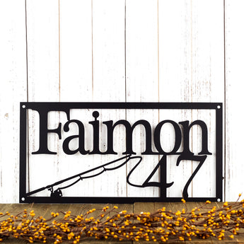 Rectangular family name and house number metal sign, in matte black powder coat. With fishing rod and reel.