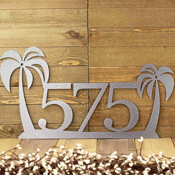 3 digit metal house number sign with palm trees, in silver vein powder coat. Placed against a wood wall.