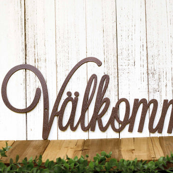 Close up of script lettering on our Välkommen metal wall art, in copper vein powder coat.