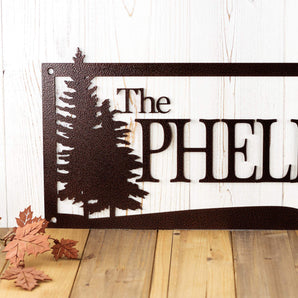 Close up of pine trees on our rectangular family name custom metal sign, in copper vein powder coat.