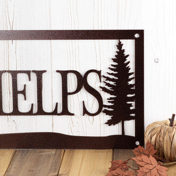 Close up of pine trees on the rectangular family name metal sign, in copper vein powder coat.