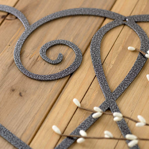 Close up of silver vein powder coat on our curly hearts metal sign. Placed on a wood plank.