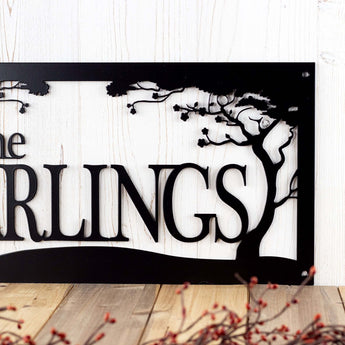 Close up of metal family last name sign with cherry trees, in matte black powder coat.