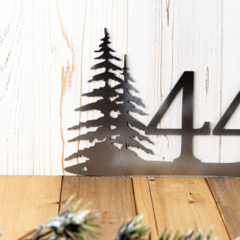 Close up of pine trees on our 3 digit metal house number sign, in raw steel.