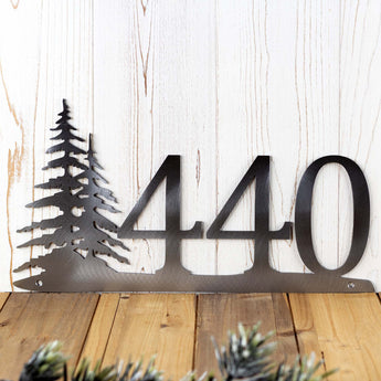 Close up of 3 digit metal house number sign with pine trees, in raw steel. 