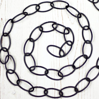 Black metal chain positioned in a spiral, on a white wood board.