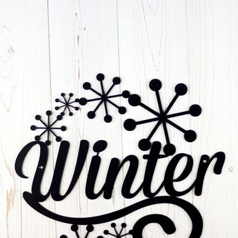 Close up of snowflakes on our Winter sign, in matte black powder coat. Placed against a white wood wall.