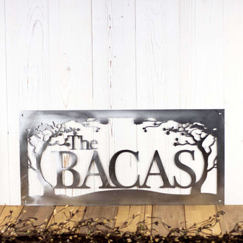 Rectangular metal family name sign with cherry trees, in raw steel. 