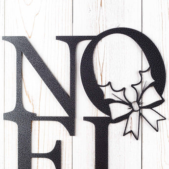 Close up of Noel metal plaque with holly and Christmas bow, in silver vein powder coat.