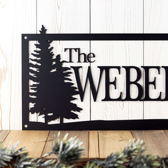 Close up of family last name on this rectangular pine trees metal plaque, in matte black powder coat. 