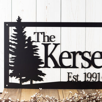 Close up of pine trees on our family last name and established year metal sign, in matte black powder coat.