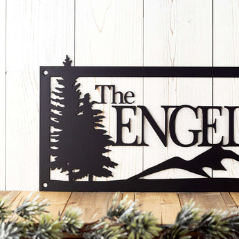 Close up of pine trees on our rectangular metal family name sign, in matte black powder coat. 
