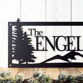 Close up of rectangular family name sign with pine trees and mountains, in matte black powder coat.