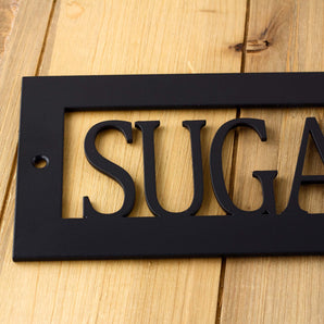 Close up of matte black powder coat on our rectagnular hanging custom cabin name metal plaque.