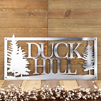 Rectangular metal home name sign, with pine trees, in raw steel. 