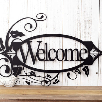 Oval welcome metal sign with vines and fleur de lis, in matte black powder coat. 