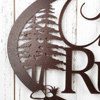 Close up of pine trees on our oval metal family name sign, in copper vein powder coat.