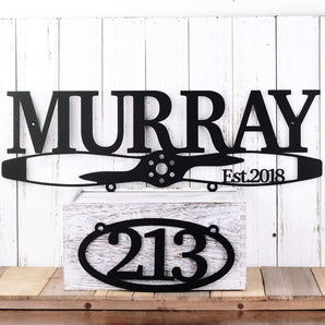 Aviator propeller family name metal sign with oval house number, in matte black powder coat.
