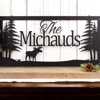 Rectangular custom family name metal sign with a moose silhouette and pine trees, in matte black powder coat.