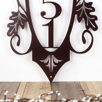 Close up of vertical metal house number sign with a fleur de lis, in copper vein powder coat.