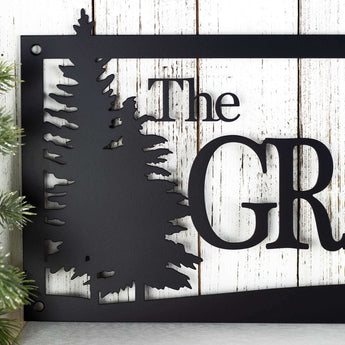 Close up of pine trees on our rectangular family name custom metal sign, in matte black powder coat.