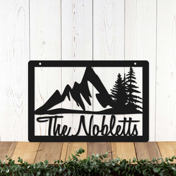 Rectangular metal family name sign with mountains and pine trees, in matte black powder coat. 