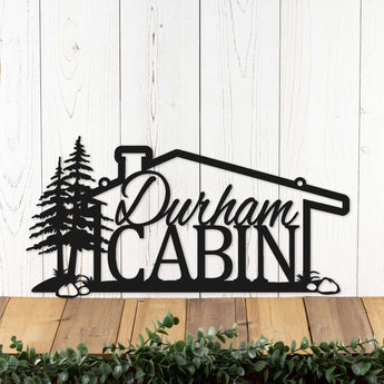 Metal family name sign with cabin and pine trees, in matte black powder coat.