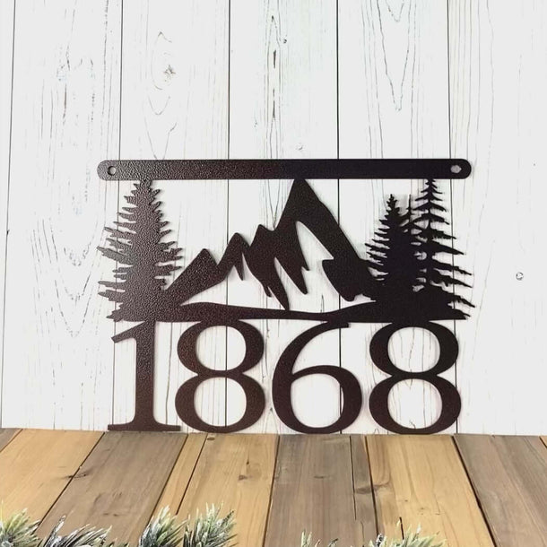Video of hanging metal house number sign with mountains and pine trees, in copper vein powder coat.