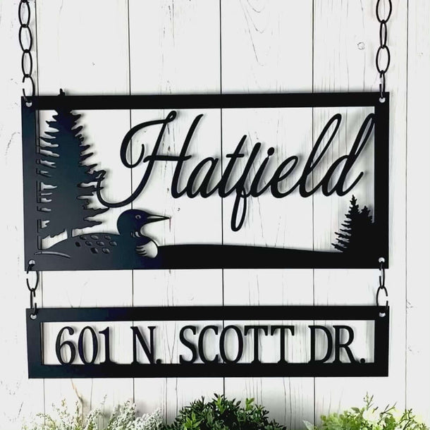 Video of cursive family name and address metal signs with a lake loon and pine trees, in matte black powder coat.